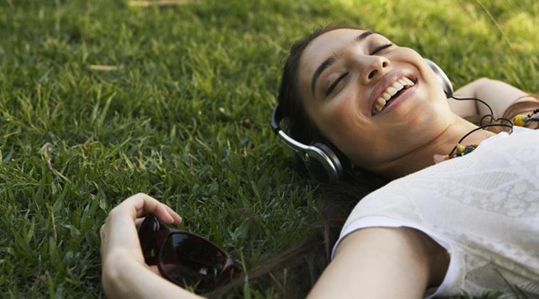 Young woman lying on grass, wearing headphones, smiling